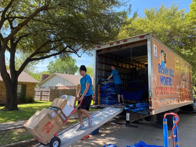 Movers unloading a Brown Box Movers truck in a shaded driveway