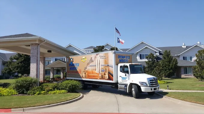 Brown Box Movers truck in front of a home flying a Texas flag