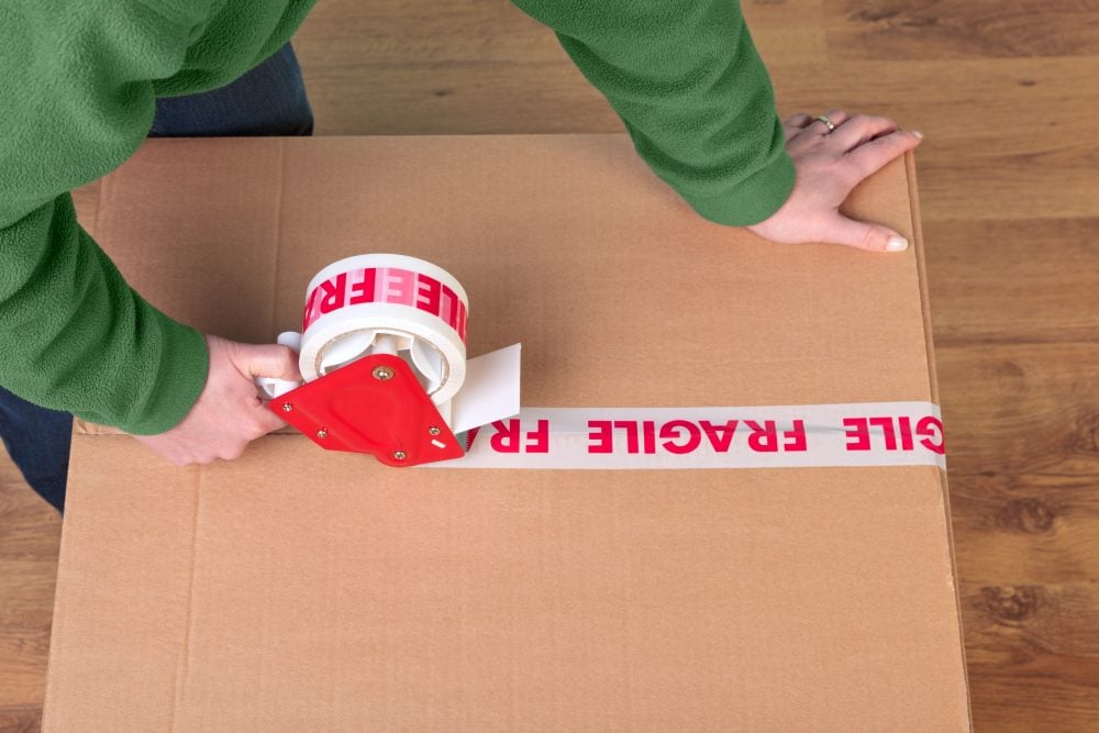 Hands sealing a moving box with fragile packing tape