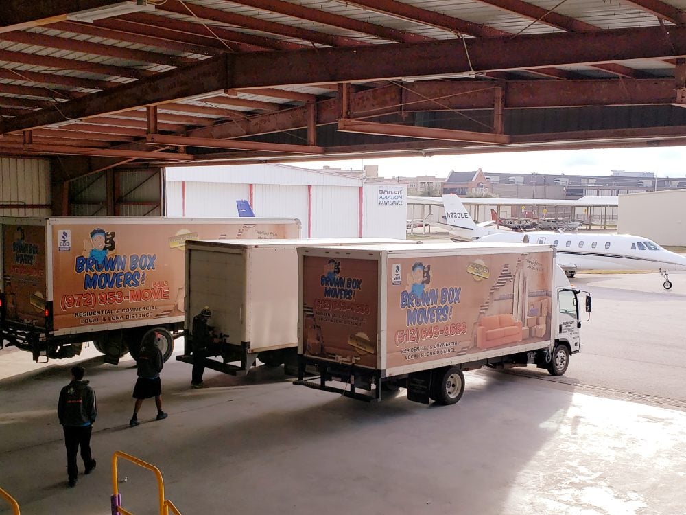 Two Brown Box Movers trucks under a covered loading area