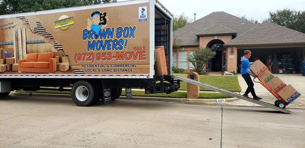 Brown Box Movers truck in a driveway as a mover unloads with a dolly