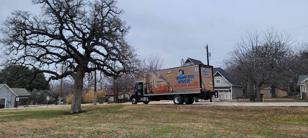 Brown Box Movers truck parked on a residential street beside a large oak tree