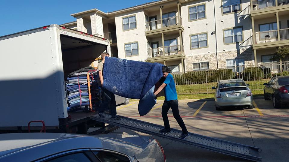 Mover unloading blanket-wrapped furniture from a truck at an apartment complex