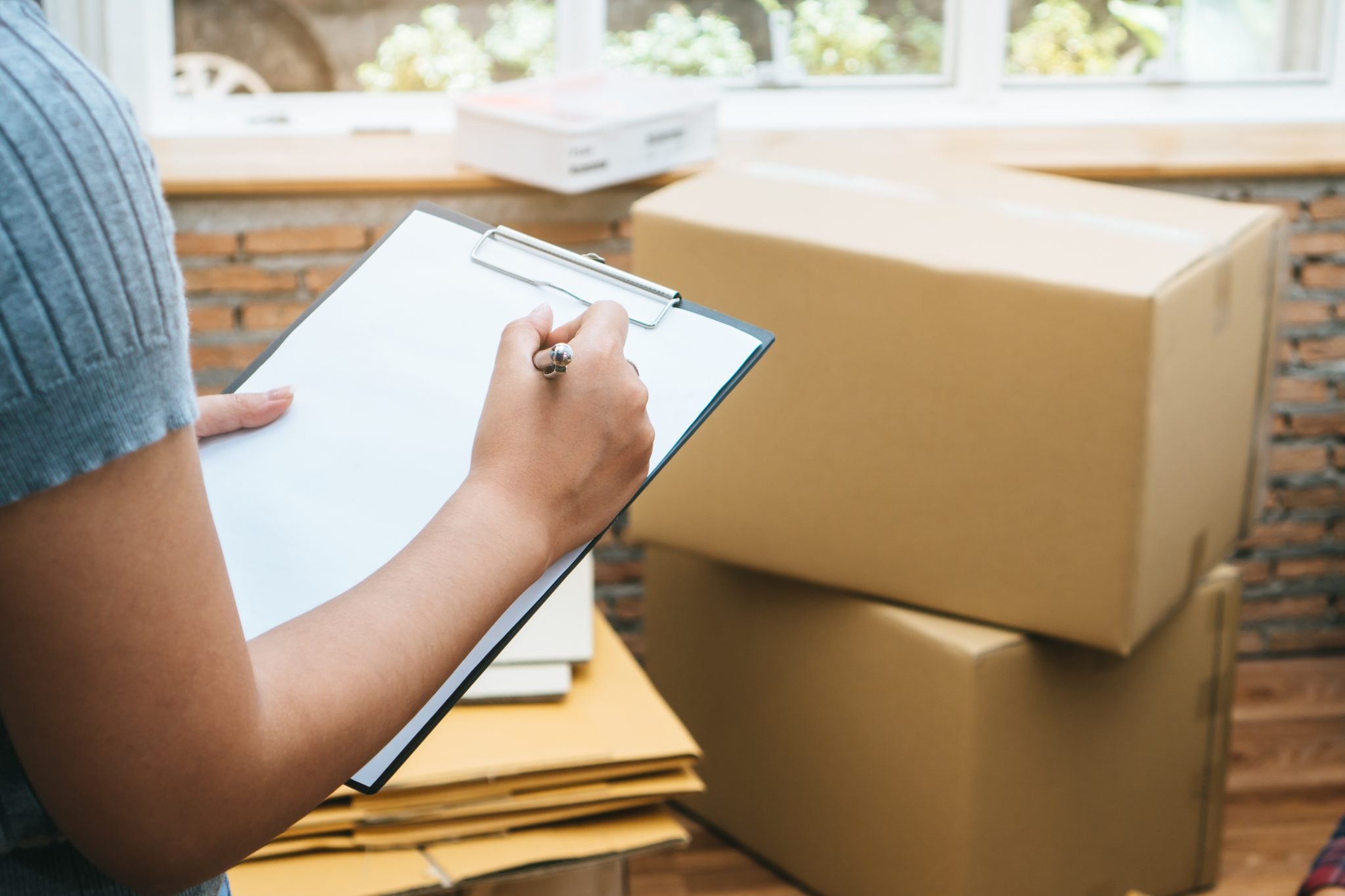 Person checking off a moving to-do list on a clipboard next to boxes