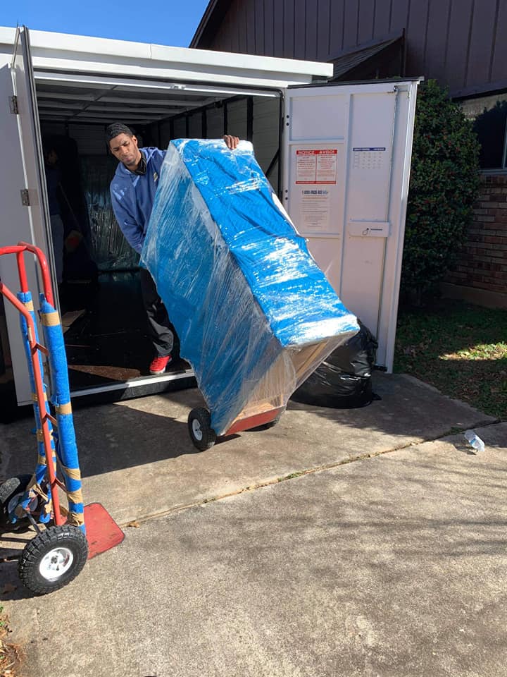 Mover rolling blanket-wrapped furniture down a truck ramp