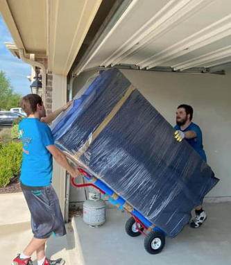 Two movers using an appliance dolly to move a wrapped refrigerator