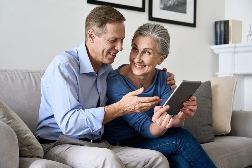 Smiling retired couple relaxing on the couch with a tablet